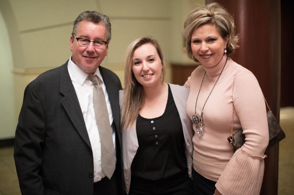 A graduate student posing for a photo with her parents at the reception